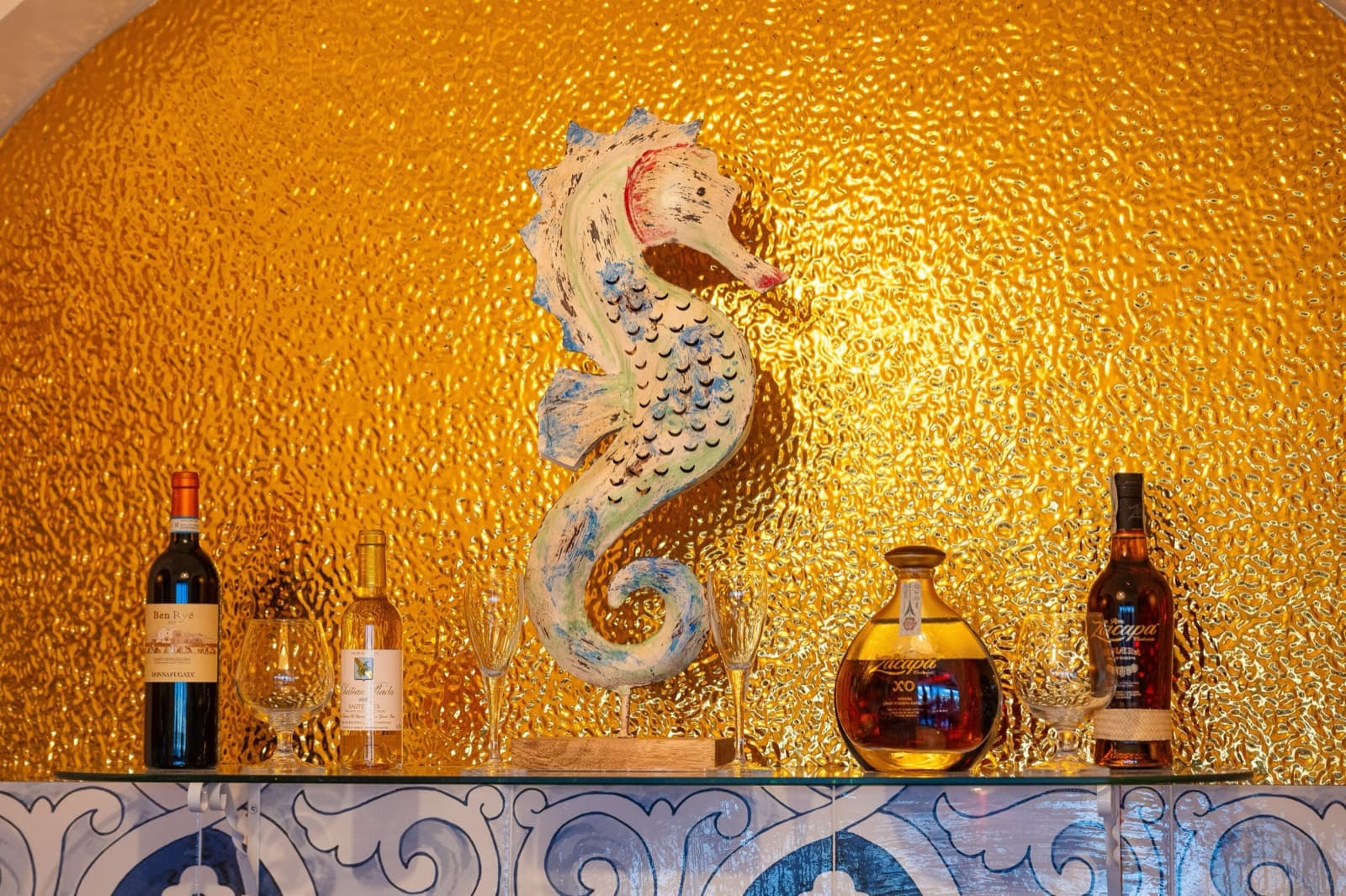 Scultura di cavalluccio marino dipinta a mano sul vetro dorato del bar, tra bottiglie di vino e rum