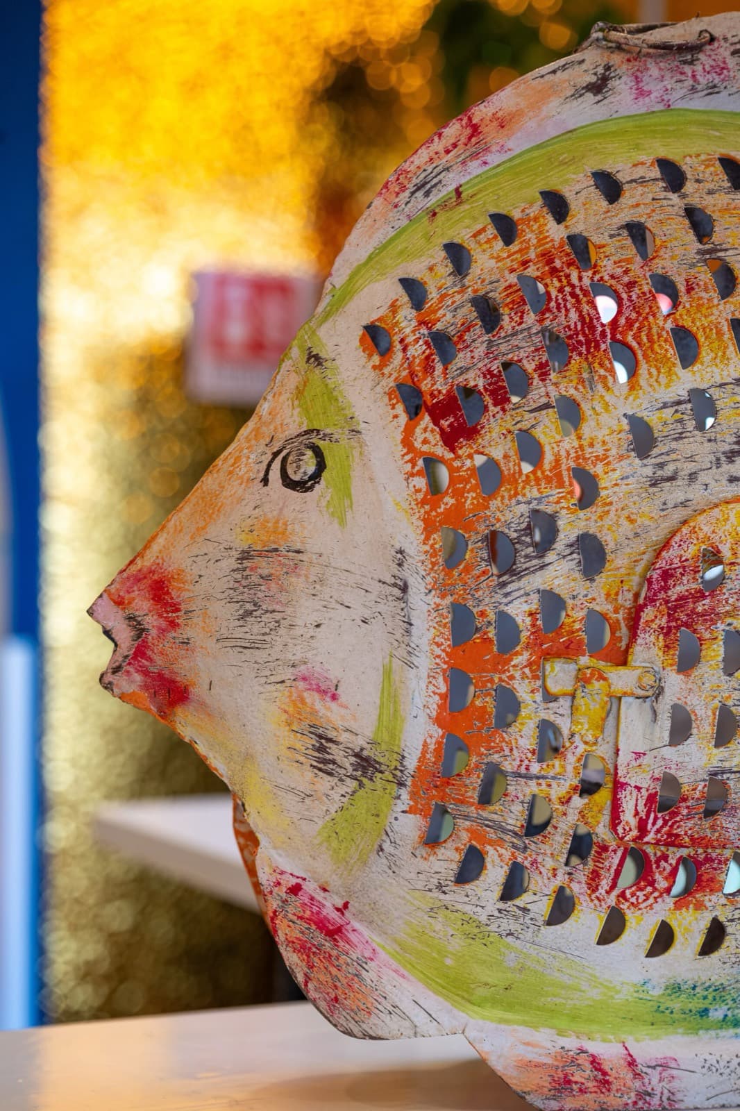Scultura di pesce dipinta a mano davanti al vetro dorato del bar
