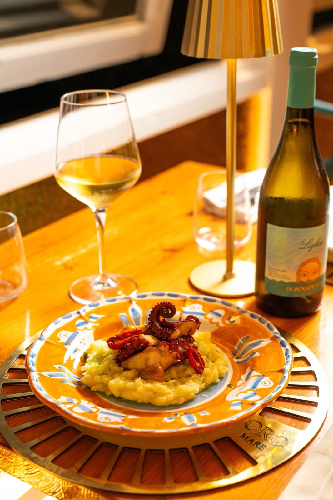 Polpo e patate servito sul piatto di maiolica firmato Oro Mare, con calice di vino bianco